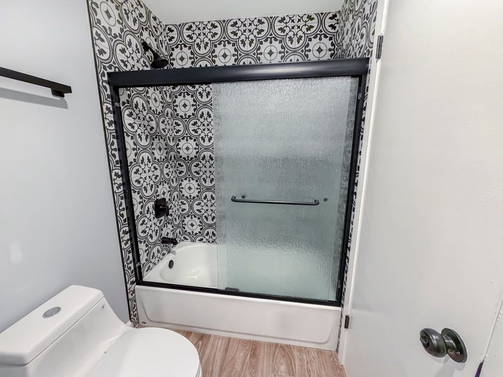 Baño terminado con azulejo decorativo alrededor de la tina y puerta corrediza de vidrio
