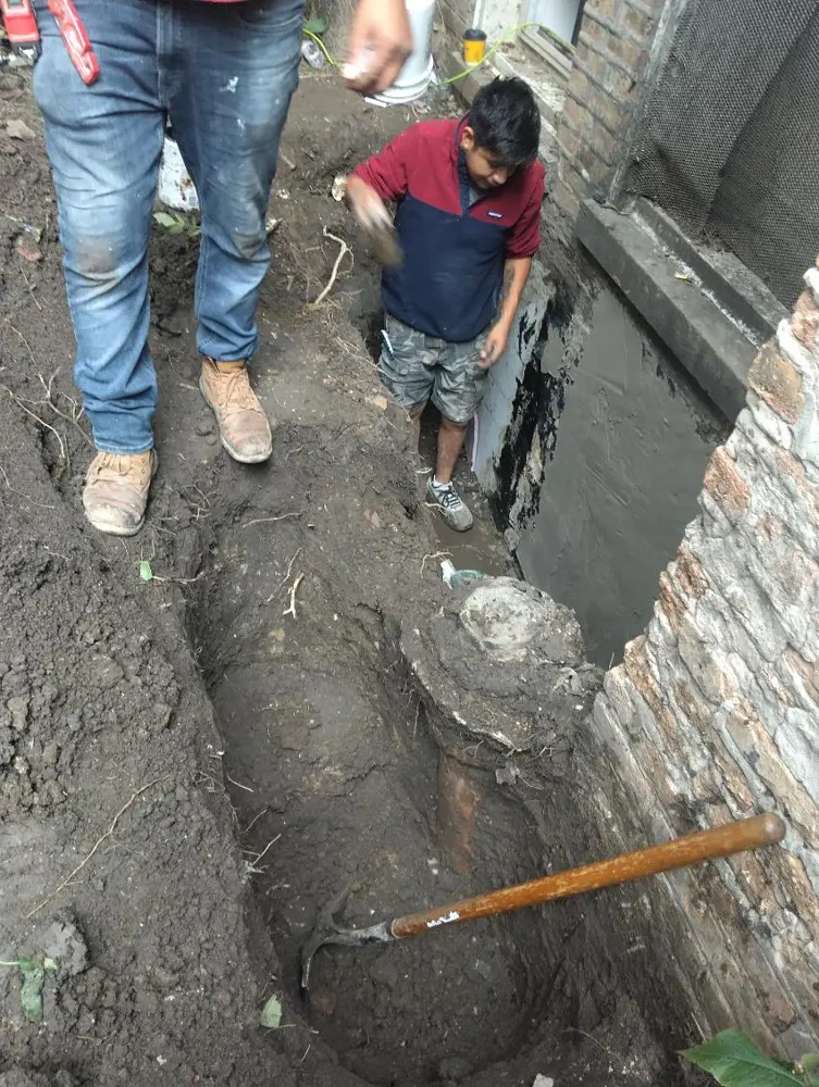 Dos trabajadores en una excavación junto a un muro de ladrillo