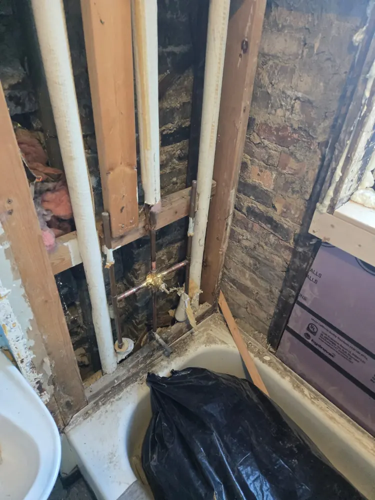 Pared abierta que muestra la estructura de madera y las tuberías detrás de un baño